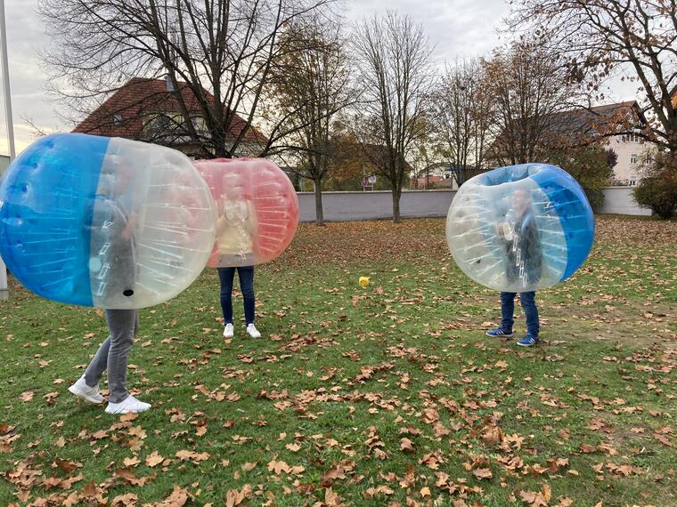 Drei Jugendliche die in Bubble Soccer Bällen stecken spielen Fußball auf einer Wiese