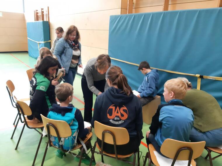 Man sieht Jugendliche, die im Halbkreis auf Stühlen sitzen und zusammen Lieder aus der ganzen Welt singen