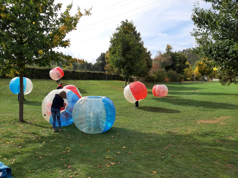 Kinder in BubbleSoccer Bällen rollen über die Wiese