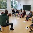 Auf dem Bild sieht man Kinder und Jugendliche, welche zum Teil auf Stühlen, zum Teil auf Cajons sitzen und zusammen Musik machen