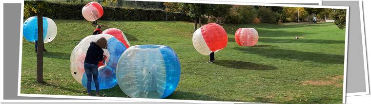 Kinder in BubbleSoccer Bällen rollen über die Wiese